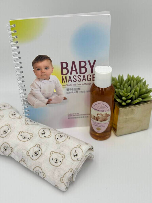 Baby massage book, towel with bear pattern, bottle of oil, and small potted plant on a white surface.