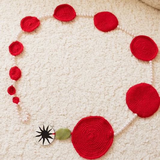 Crocheted red flower and yarn on a textured beige surface