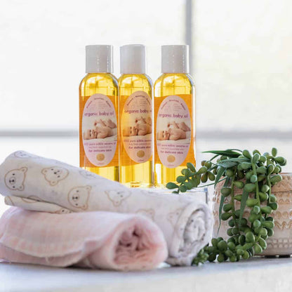 Three bottles of organic baby oil with towels and a plant on a light background